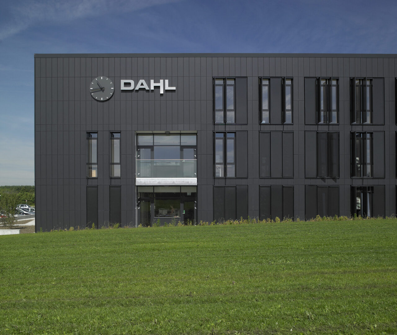 Gebäude der Anwaltskanzlei Dahl in Viborg mit modernen schwarzen Keramikpaneelen, großen Fenstern und einem Uhrenschild an der Fassade, umgeben von einer gepflegten Grünfläche