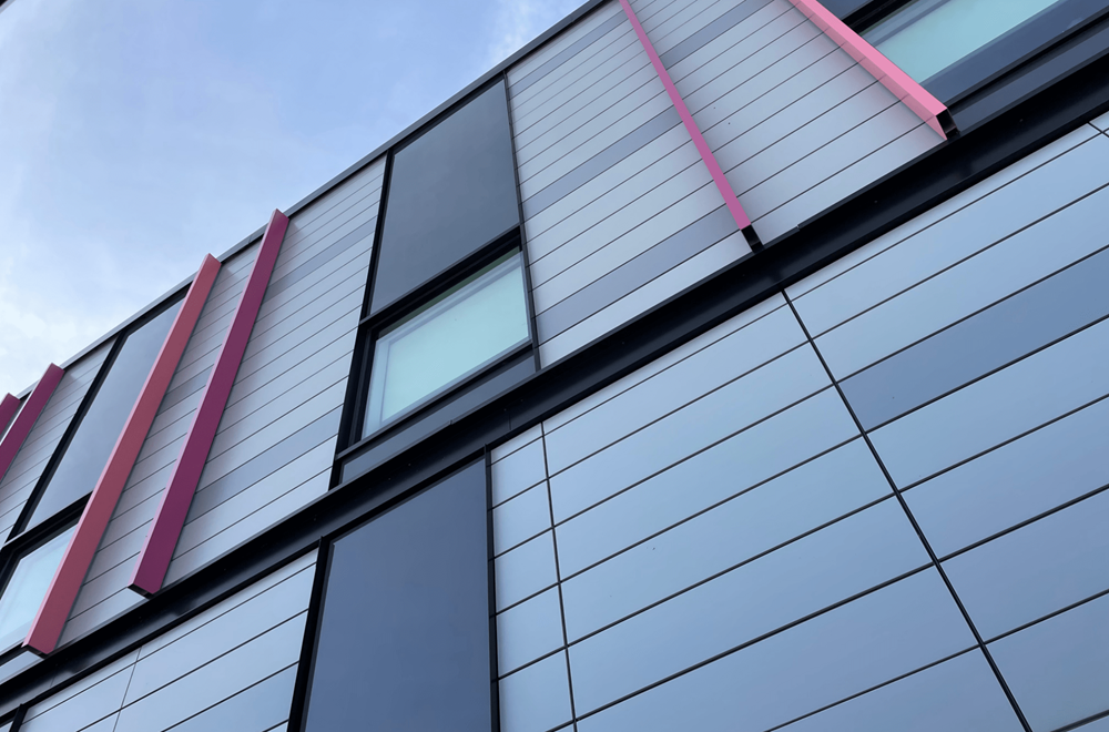 Fassade eines modernen Gebäudes mit vertikalen roten Akzenten und reflektierenden Glasflächen unter blauem Himmel.